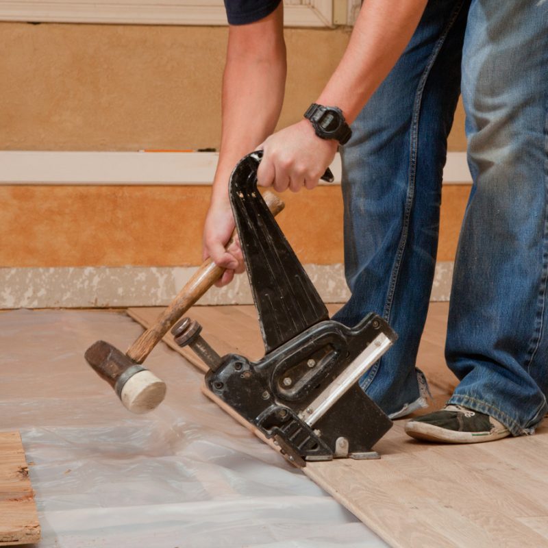 Worker,Uses,Pneumatic,Hardwood,Nailer,On,A,New,Floor,Installation.